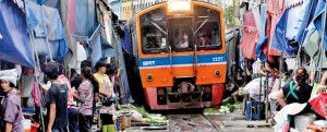 Thai vegetable market vendors pull back awnings and their produce off a railway track to allow a cross-country train to dissect through the middle of the town of Maeklong, in Samut Songkhram