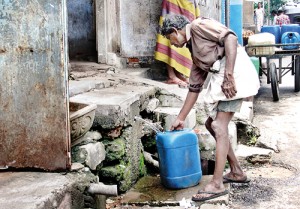 A vendor collects water at a filthy spout. In the background are more cans ready to be filled...for you and me?