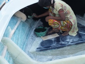 Tharmalingam Tharnam, crouched and painting the front inside of a fibre-glass boat under construction; The boats manufactured at  Jayapuram, Kilinochchi lined up for distribution to fishermen of Poonakari