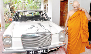 The chief monk stands besides one of the damaged vehicles