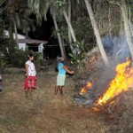 A young woman lights a fire beside her home to keep both  elephants and mosquitoes at bay