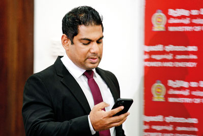Energy Minister Kanchana Wijesekera reading a just-received SMS on Wednesday as he arrived for a news conference. He told journalists that the message confirmed that 20 CPC trade union activists had been suspended.